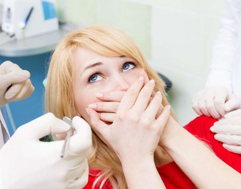 A woman anxiously sits in a dental chair as the dentist examines her teeth.