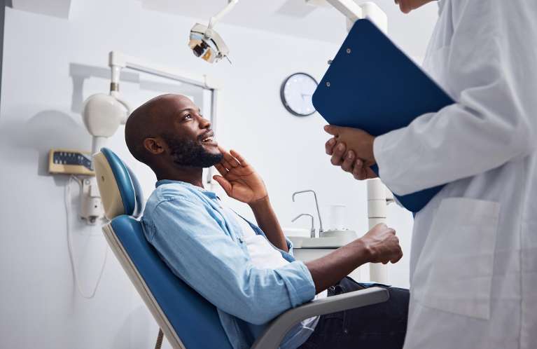 A man sitting in a chair discussing dental crowns with a doctor in a clinical setting.