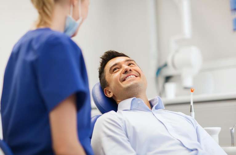 A man sitting in a dentist chair, smiling, highlighting the importance of regular dental checkups.